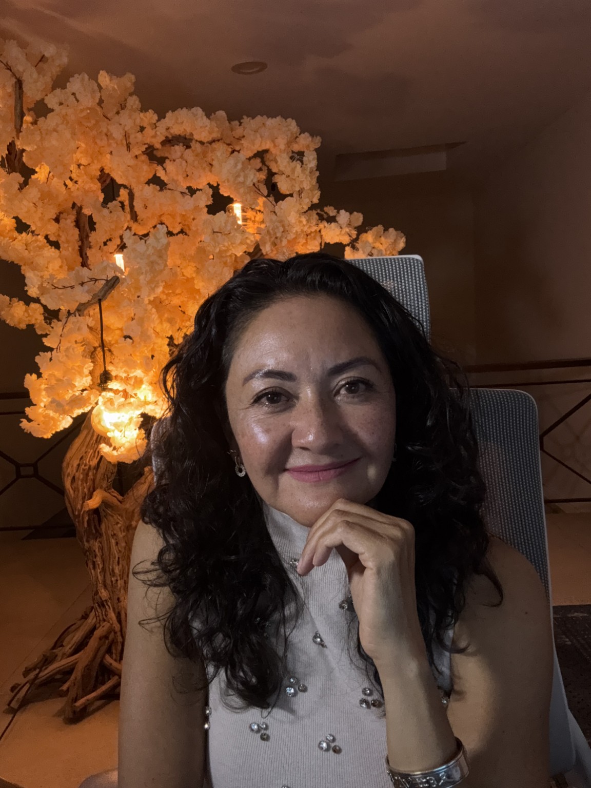 Retrato de Yolanda Carmona, sonriendo junto a un árbol de flores iluminado.